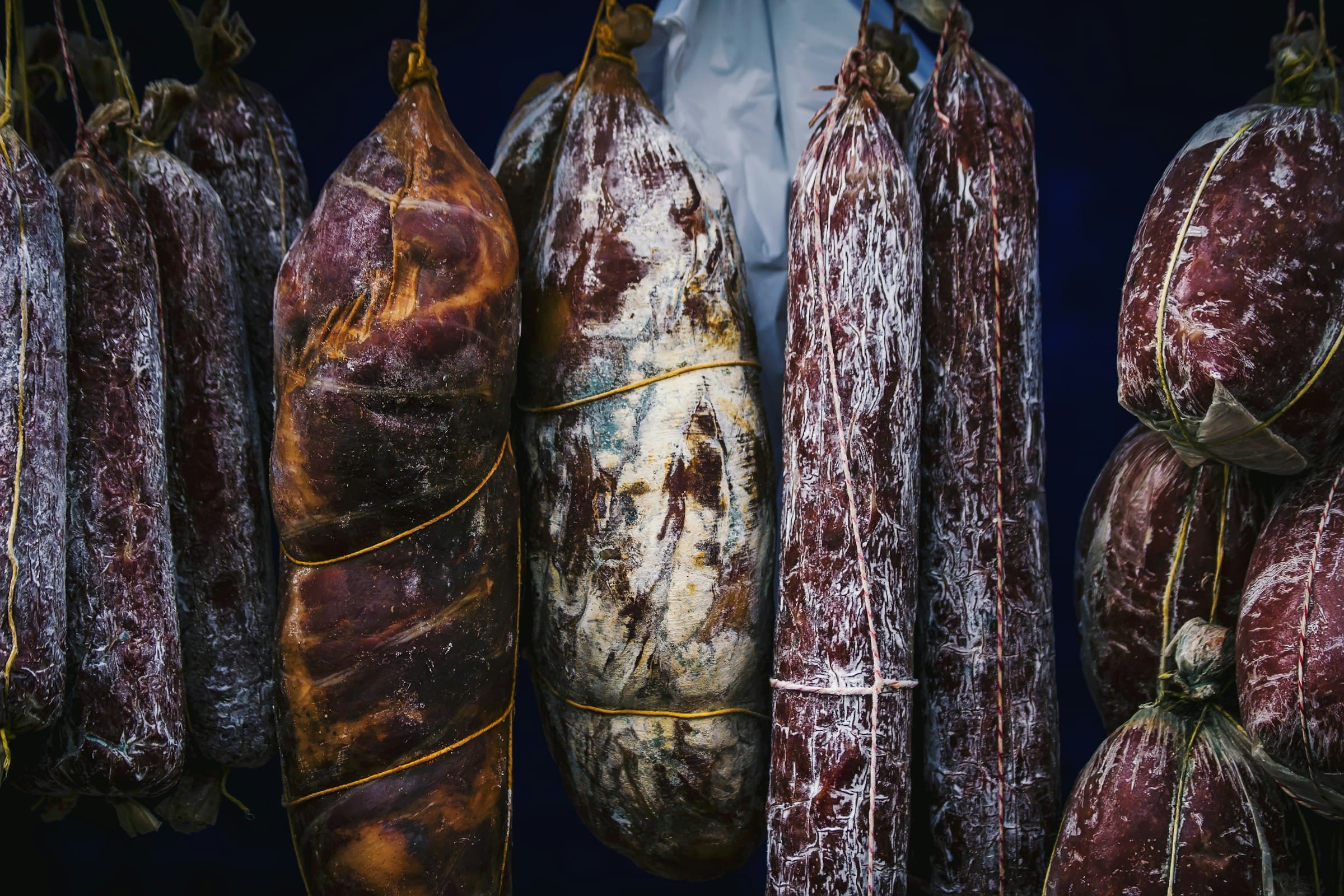 Salami and whole muscle charcuterie hanging in a curing chamber with white surface mold