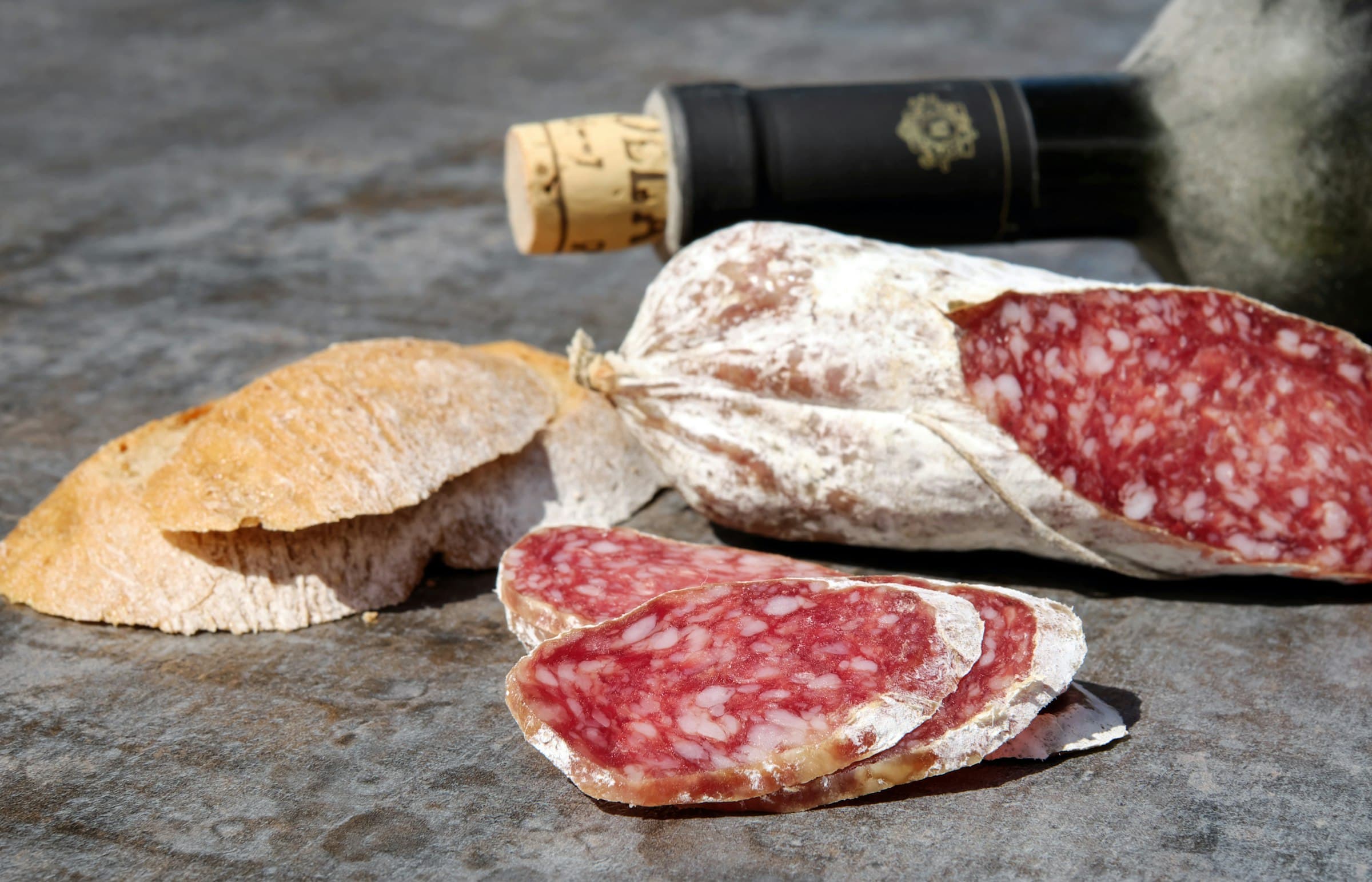 A whole dry cured salami with white bloom on the casing, sliced to show the fat and lean